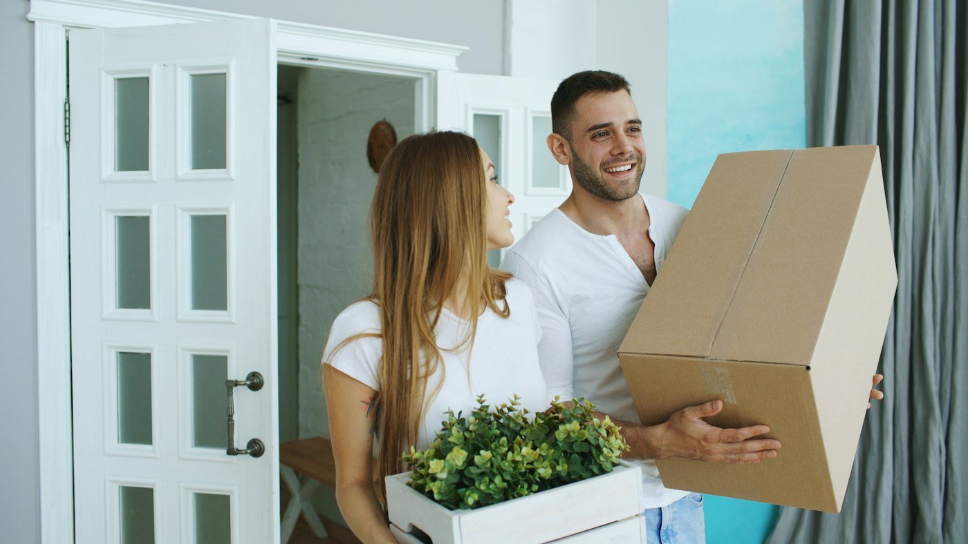Couple portant des cartons et des plantes à son arrivée dans son nouveau logement