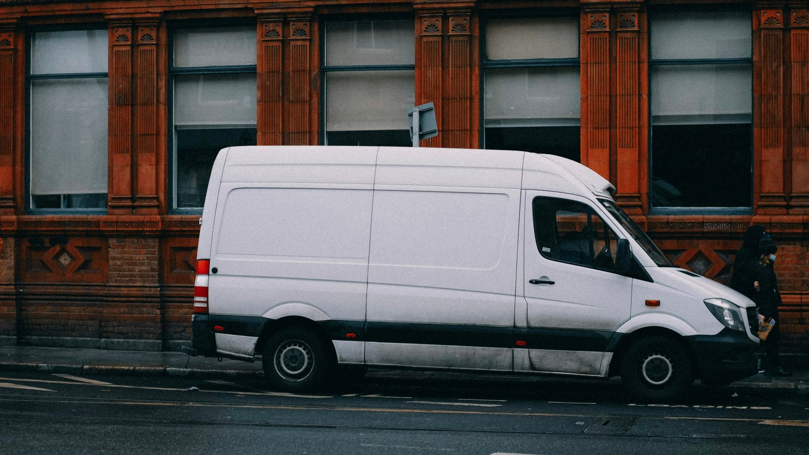 Camionnette blanche garée dans une rue, devant une façade en briques